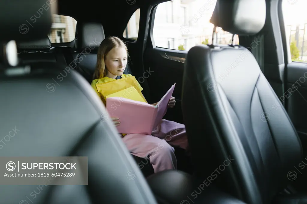 Focused girl reading book in backseat of car