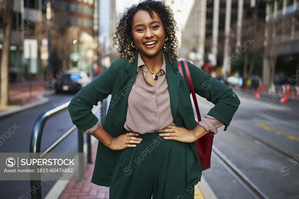 Happy young beautiful businesswoman with arms akimbo standing on street