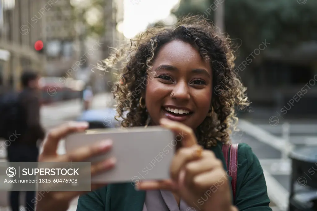 Smiling beautiful young businesswoman photographing through mobile phone