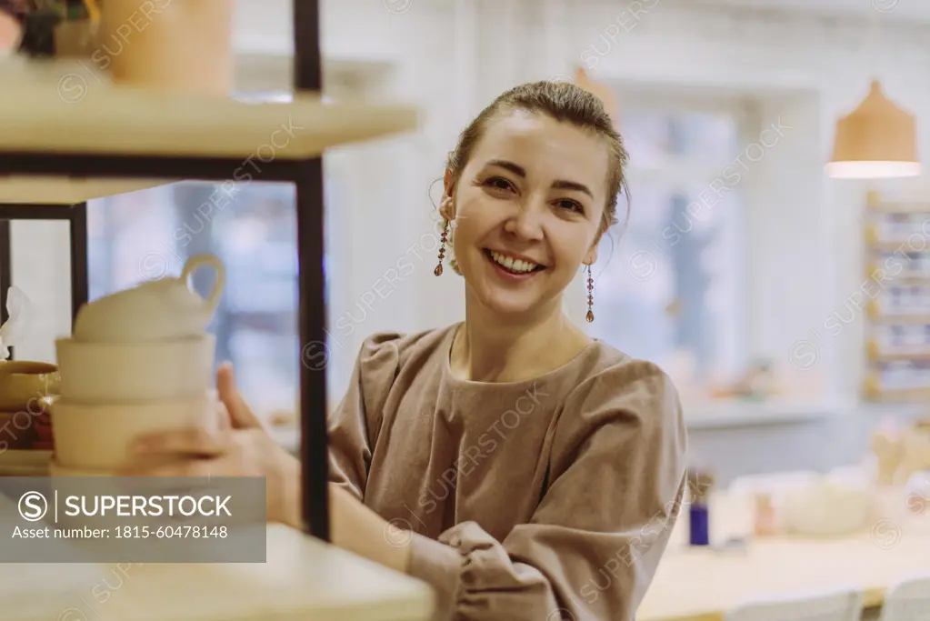 Happy businesswoman arranging handmade clay crockery in workshop