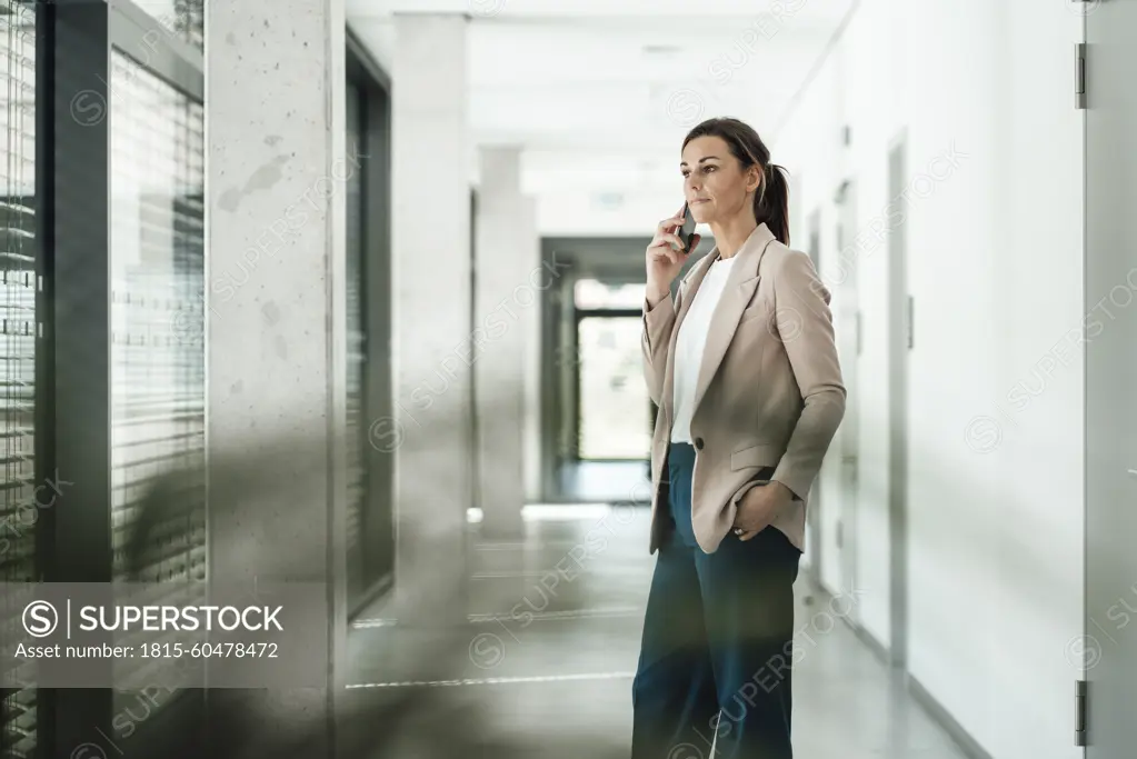 Businesswoman with hand in pocket talking on smart phone at office