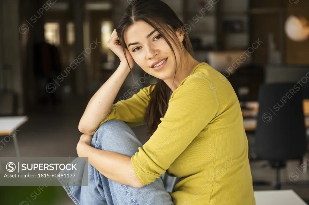 Young businesswoman with head in hand sitting on desk at work place