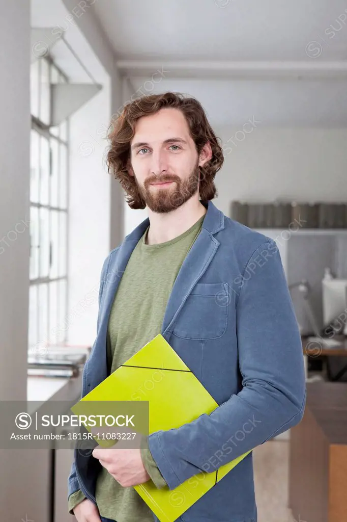 Portrait of smiling young man with file standing in an office