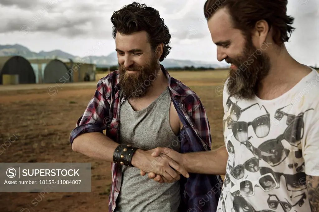 Two men with full beards in abandoned landscape shaking hands