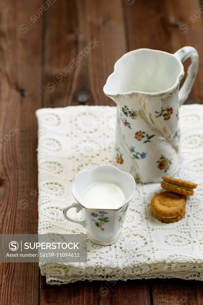 Cup of milk, milk pitcher and cookies on white tablecloth