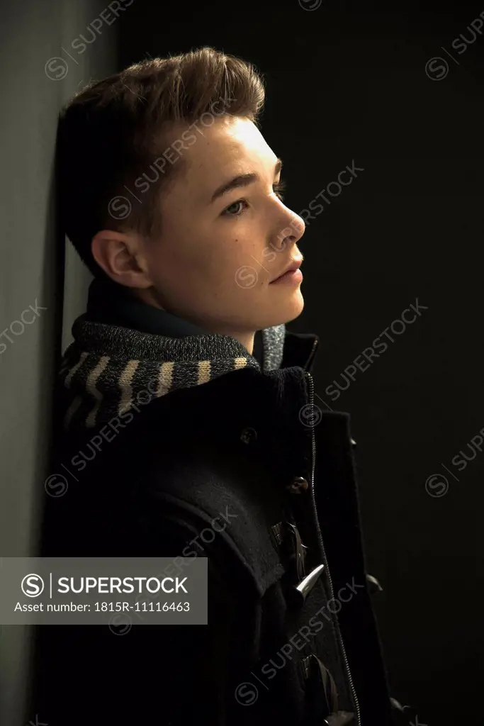 Profile of serious looking teenager leaning against black wall