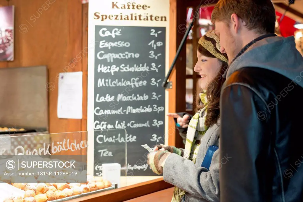 Germany, Berlin, young couple buying deep-fried pastries at Christmas market