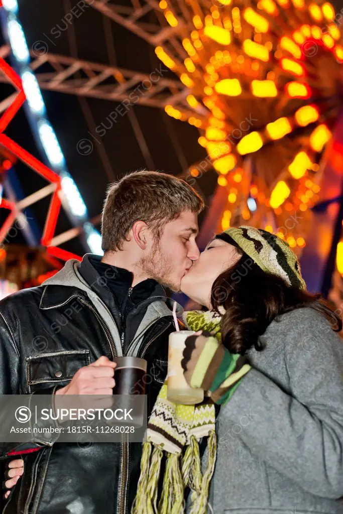 Germany, Berlin, happy young couple kissing at Christmas market in front of lighted big wheel