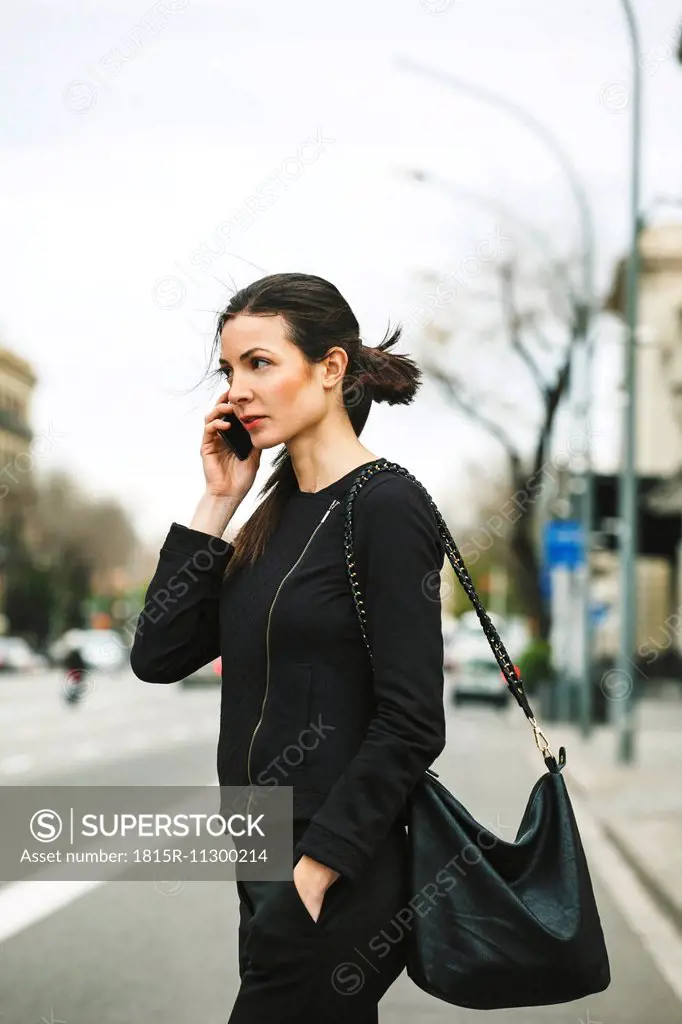 Spain, Catalunya, Barcelona, young black dressed businesswoman telephoning in front of a street