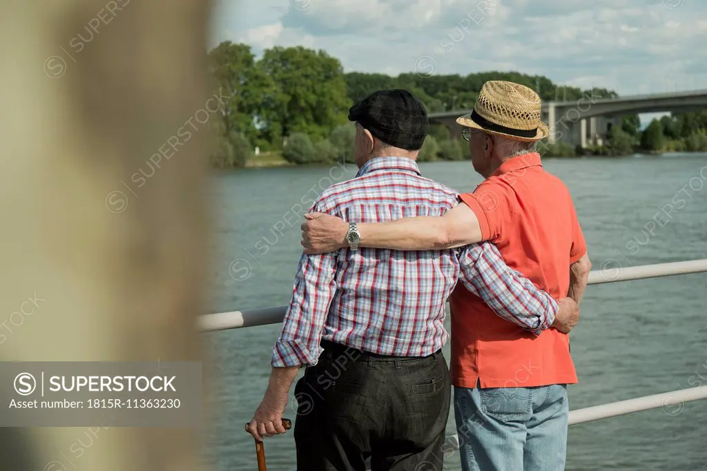 Germany, Rhineland-Palatinate, Worms, two old men standing arm in arm looking at Rhine River, back view