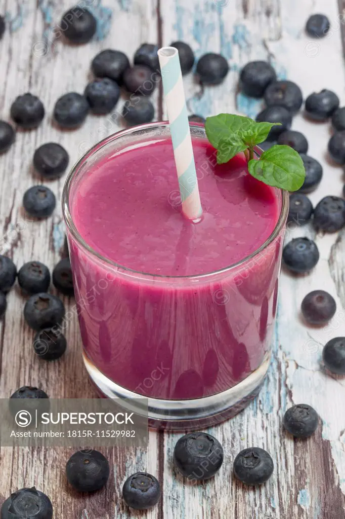 Glass of blueberry smoothie and blueberries on wood