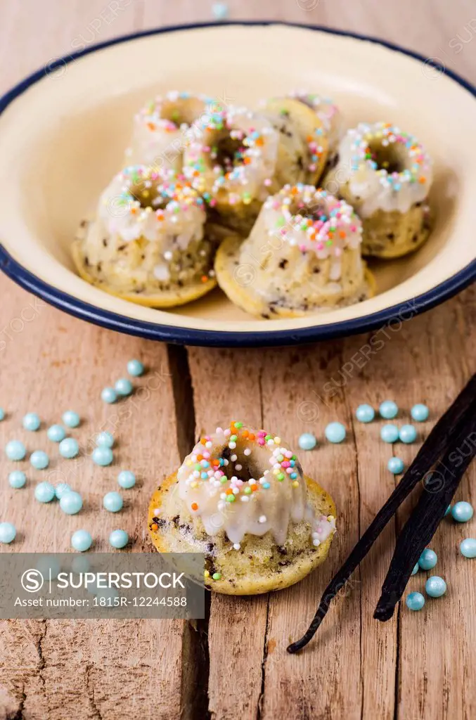 Bowl of mini vanilla marble cakes, pearls and vanilla pods on wood