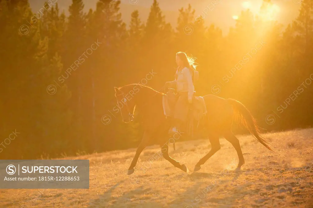 USA, Wyoming, riding cowgirl at backlight