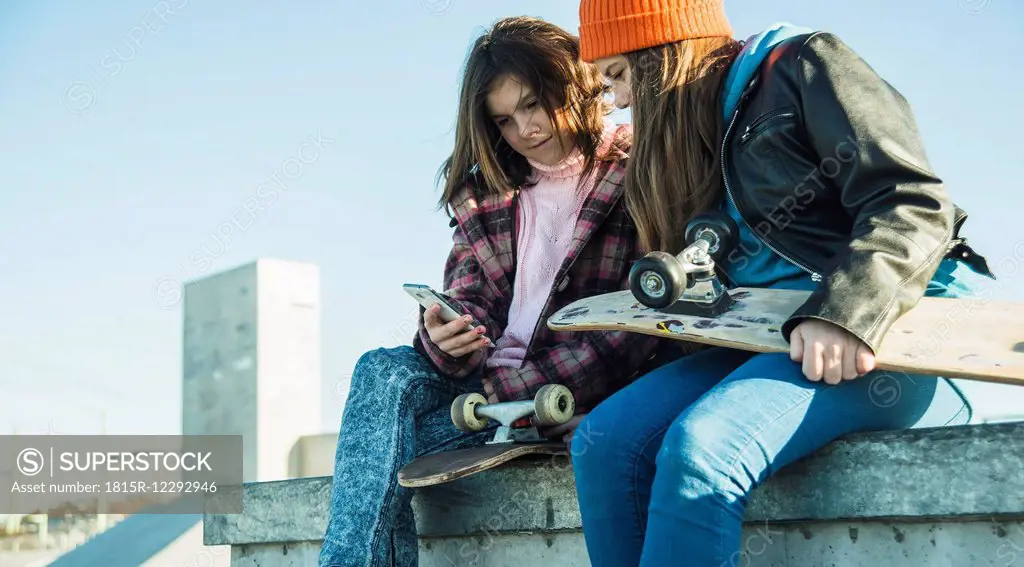 Two girls in skatepark sharing cell phone