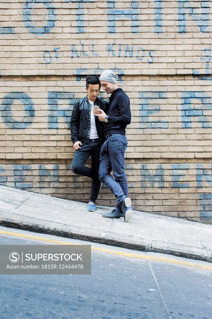 China, Hong Kong, gay couple at house wall looking on cell phone