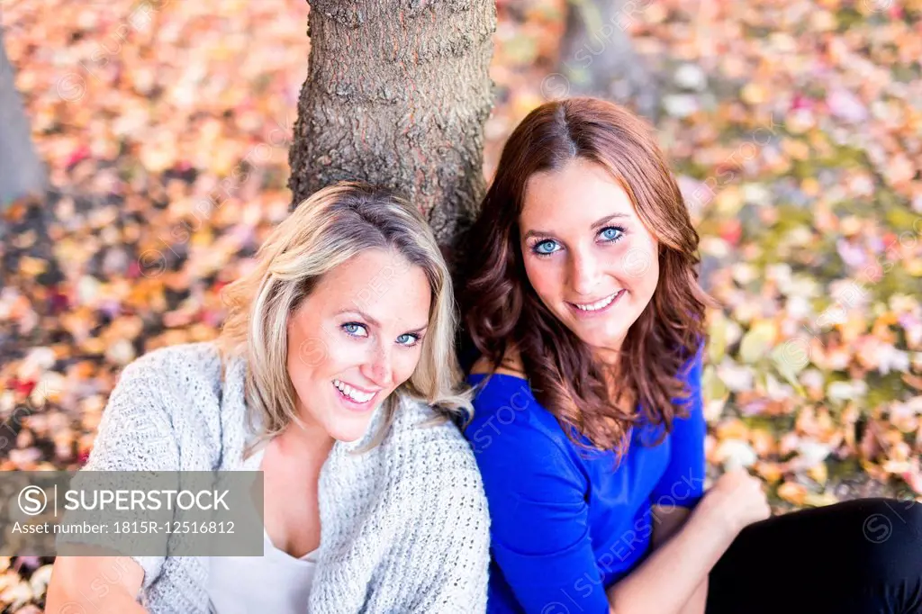 Portrait of two female friends leaning on tree trunk