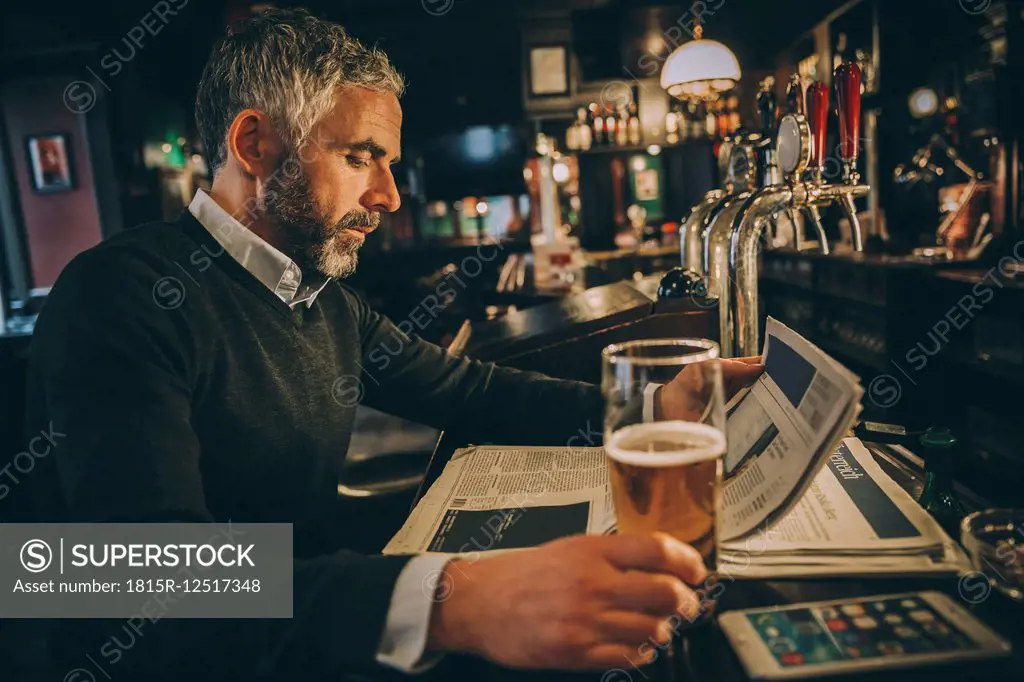 Man sitting at counter of a pub reading newspaper