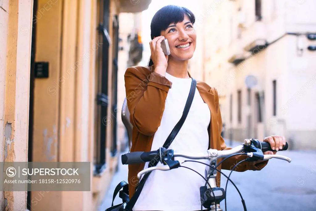 Spain, Barcelona, smiling woman with bicycle and cell phone in the city