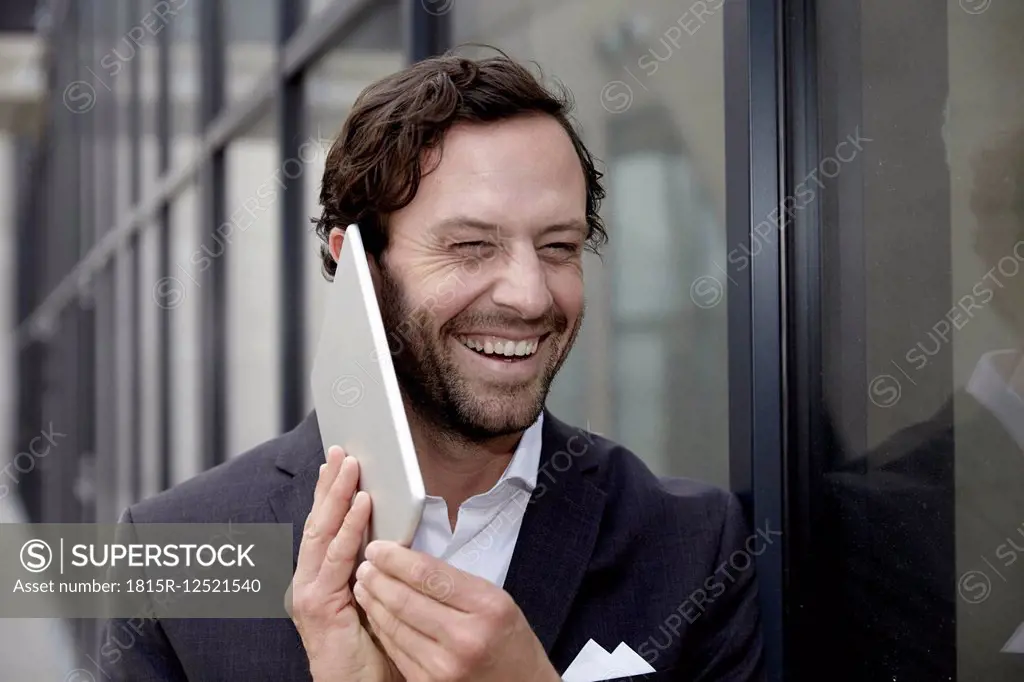 Portrait of laughing businessman trying to phone with his digital tablet