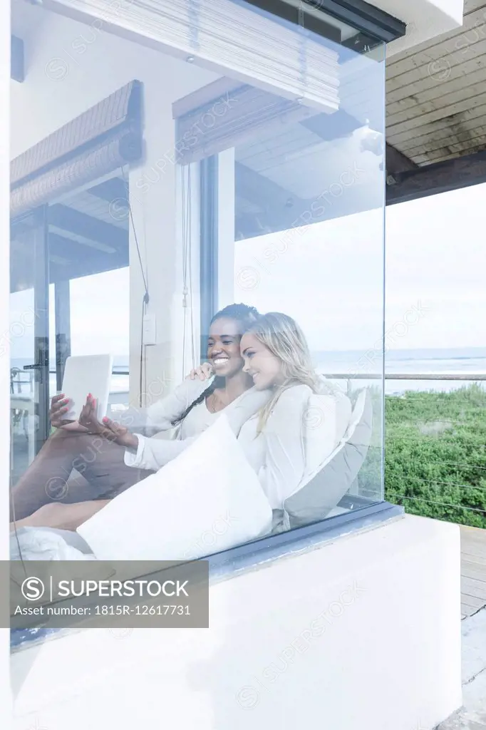 Two young women with digital tablet relaxing in beach house