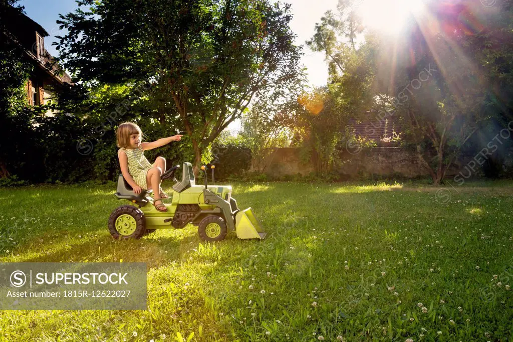 Little girl playing with toy tractor in a garden