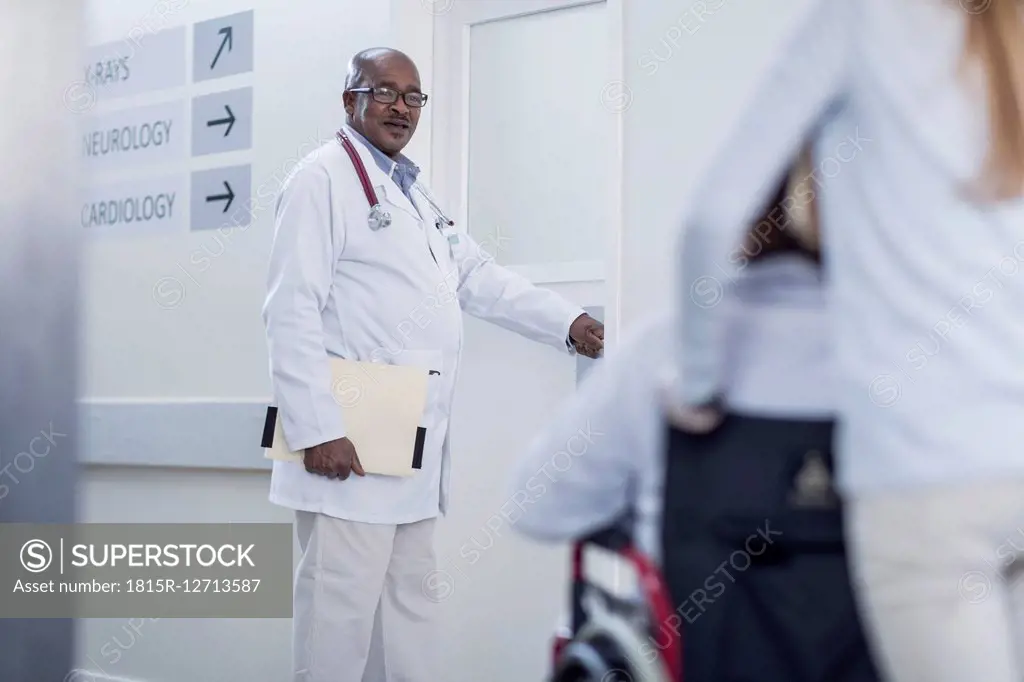 Doctor in hospital corridor opening door and patient in wheelchair