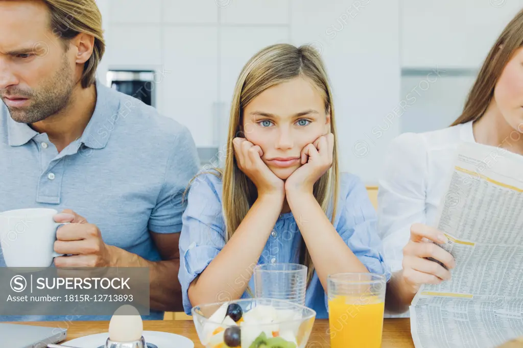 Frustrated girl with distracted parents at breakfast table