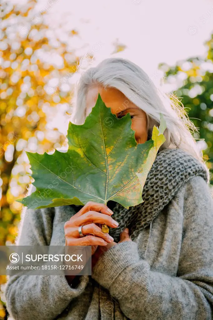 Woman hiding her face behind an autumn leaf