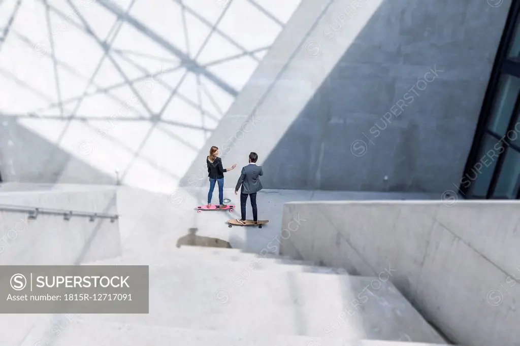 Two business people standing on skateboards in modern architecture