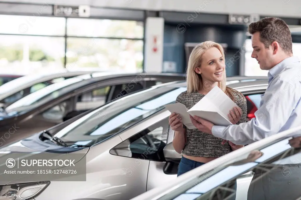 Car dealer explaining new car to young woman