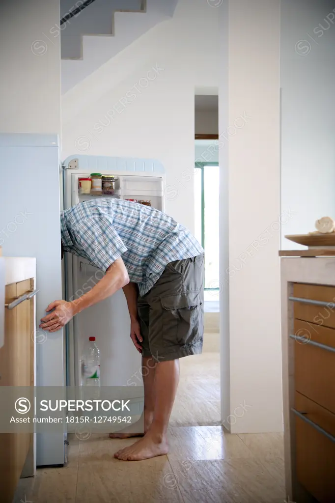 Young man standing in the kitchen searching something in the fridge