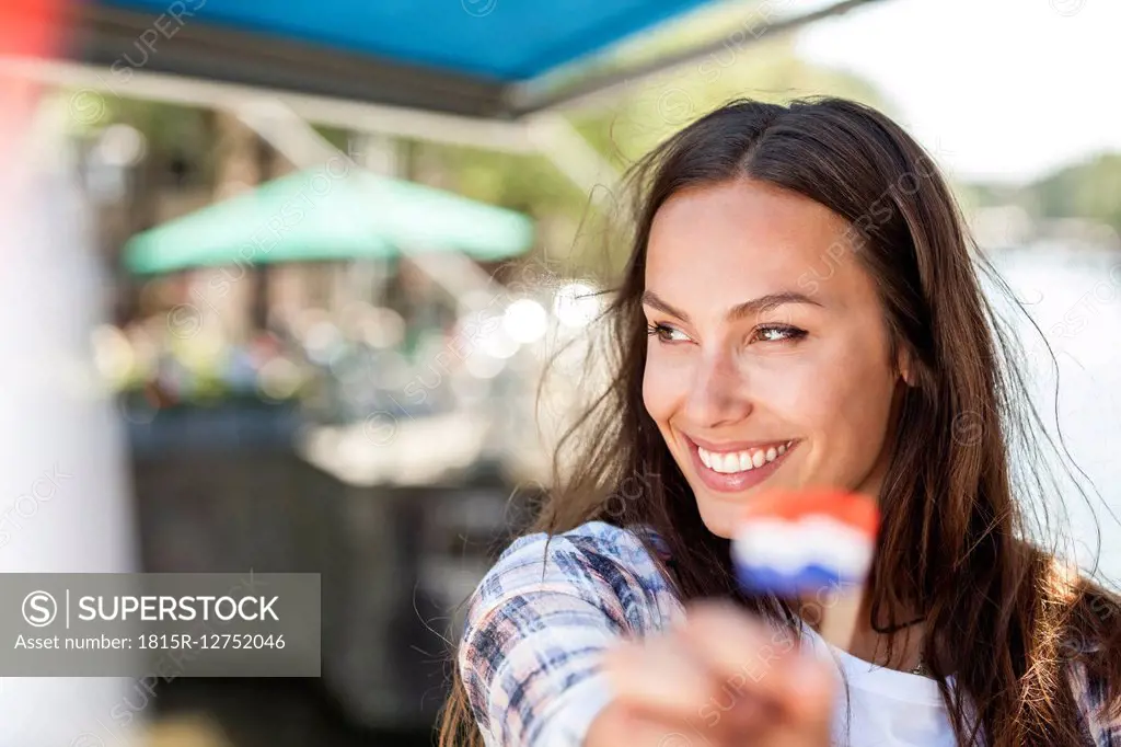 Netherlands, Amsterdam, smiling young woman holding small Dutch flag