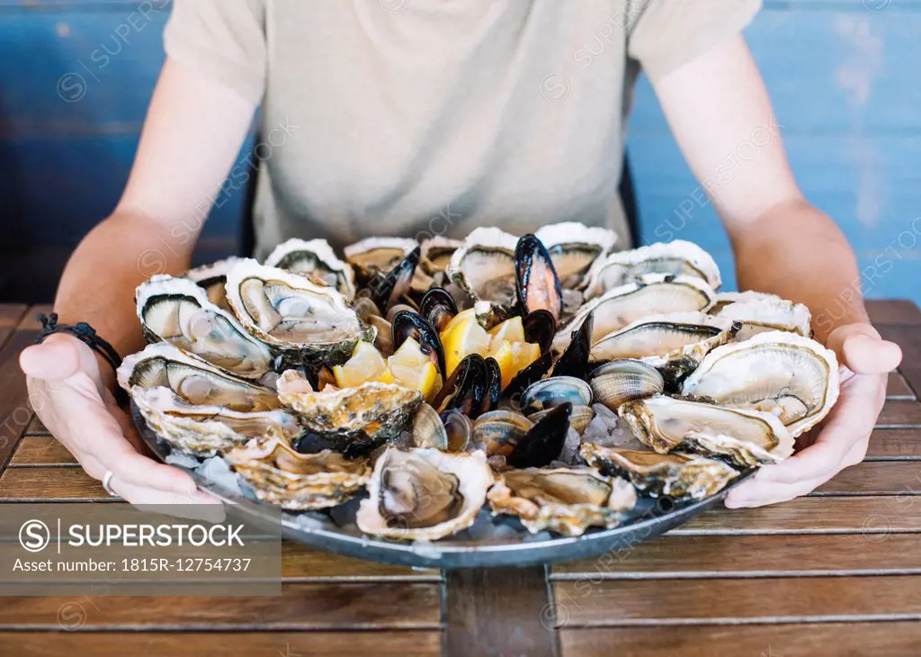 Man's hands holding a seafood platter with oysters, clams and mussels.