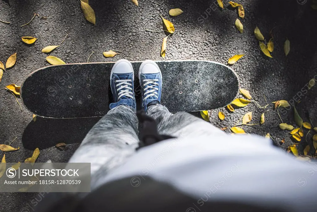 Boy standing on skateboard on path with autumn leaves