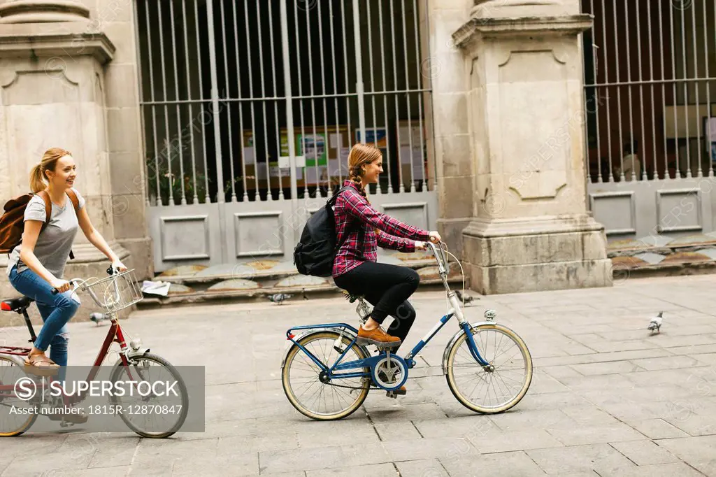 Spain, Barcelona, two young women riding bicycle in the city