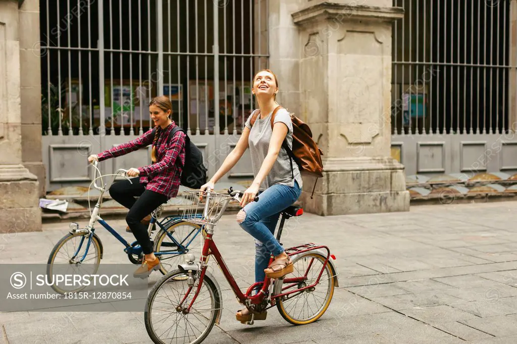 Spain, Barcelona, two young women riding bicycle in the city