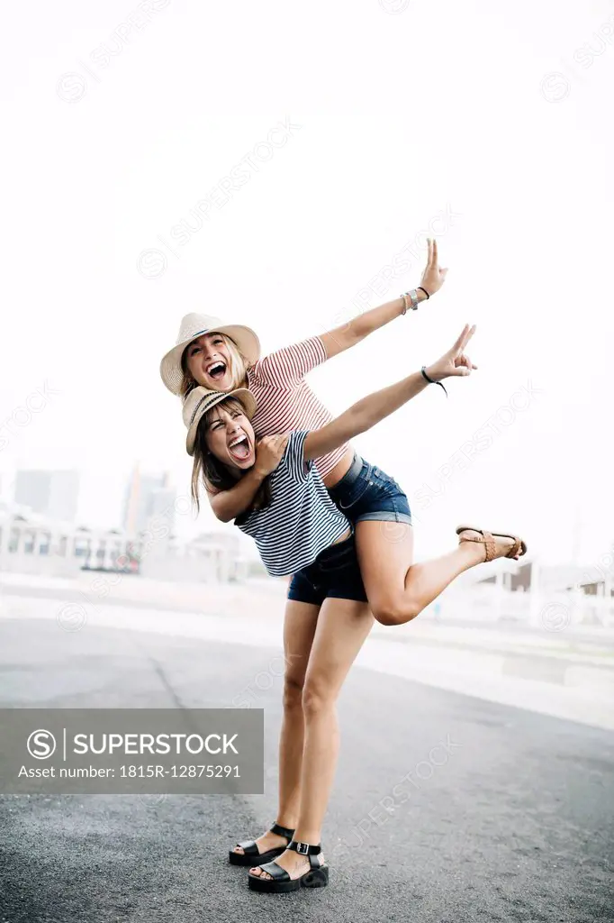 Spain, Barcelona, young woman giving her friend a piggyback ride