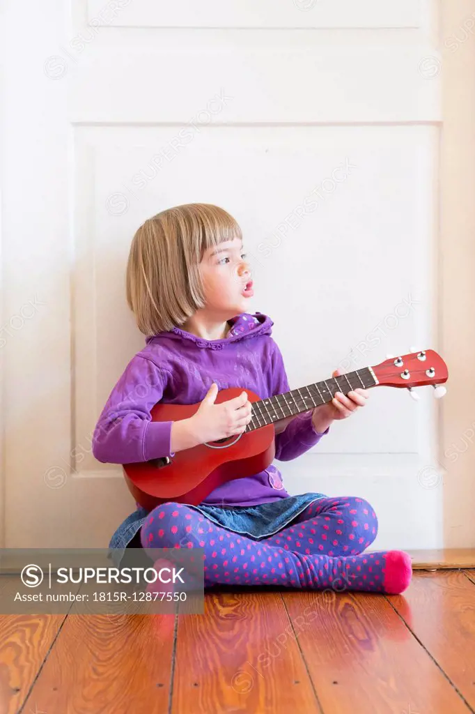 Portrait of little girl sitting on wooden floor playing ukulele