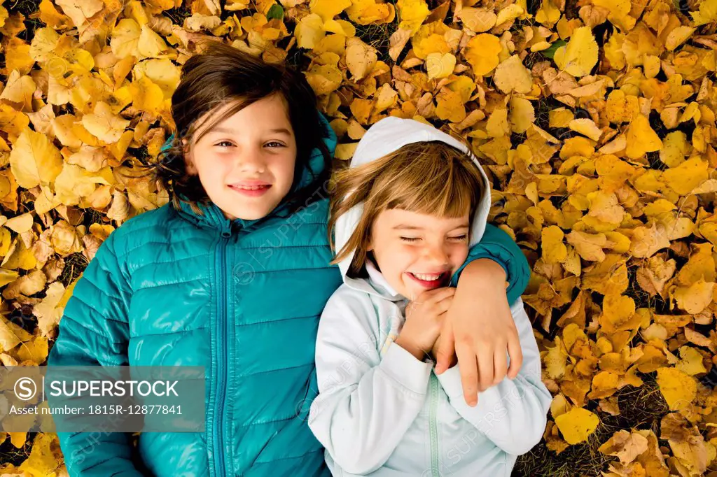 Two girls lying side by side on ground covered with autumn leaves