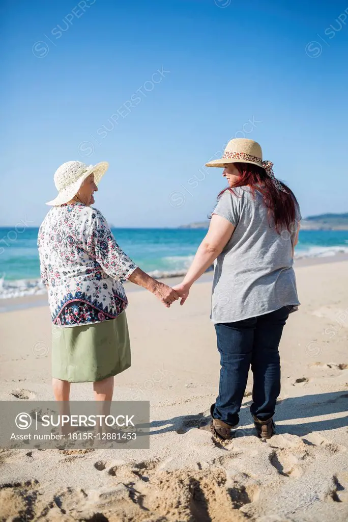 Grandmother and adult granddaughter holding hands on the beach on a sunny day