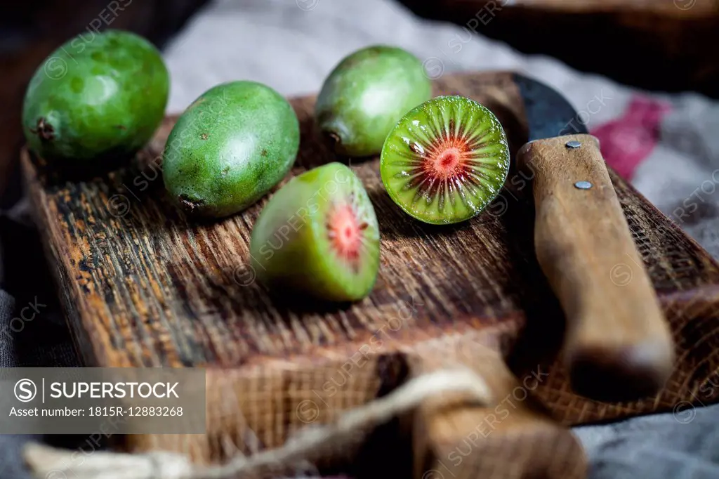 Sliced and whole mini kiwis and kitchen knife on wooden chopping board