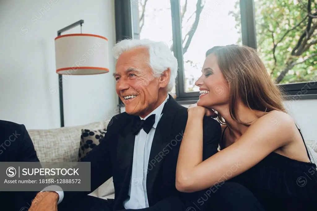 Smiling young woman with elegant senior man on couch