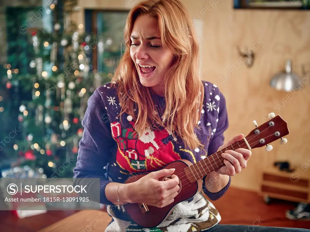 Blond woman playing ukulele in front of Christmas tree