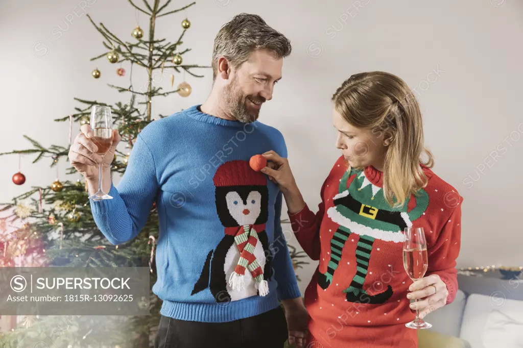 Two people with ugly Christmas sweaters laughing in front of tree