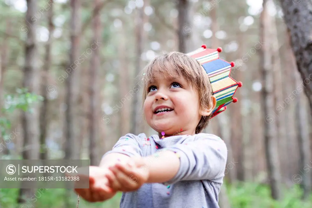 Portrait of smiling little boy wearing paper crown catching confetti