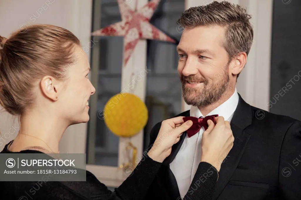 Couple preparing for New Year's Eve party, fastening bow tie