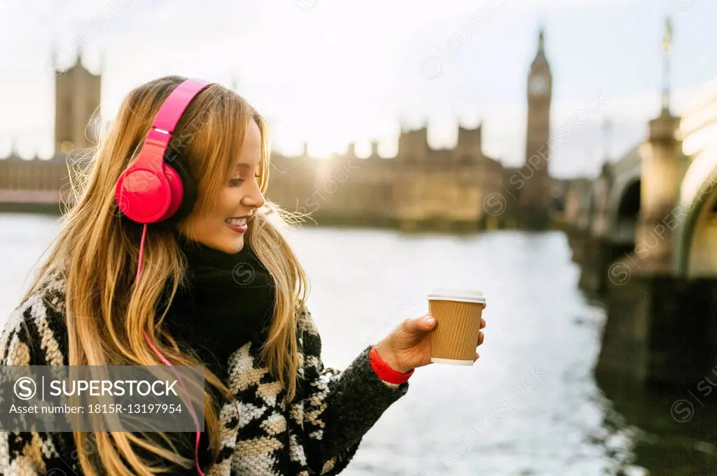 UK, London, young woman listening music and drinking coffee near Westminster Bridge