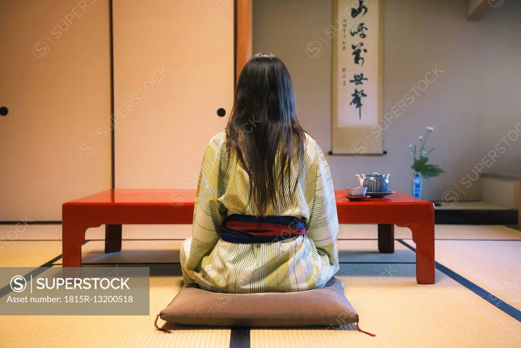 Japan, Uji, back view of woman wearing yukata drinking tea in a traditional Japanese room