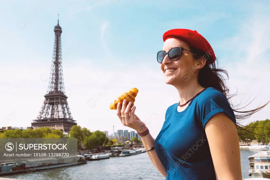 France, Paris, woman with croissant standing in front of Seine river and Eiffel Tower