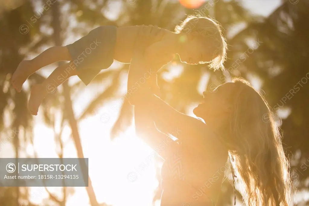 Happy mother lifting up her son in backlight